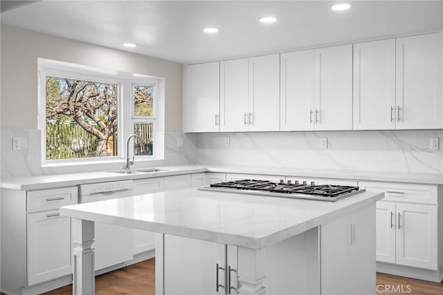 kitchen with a sink, a kitchen island, wood finished floors, stainless steel gas stovetop, and dishwasher