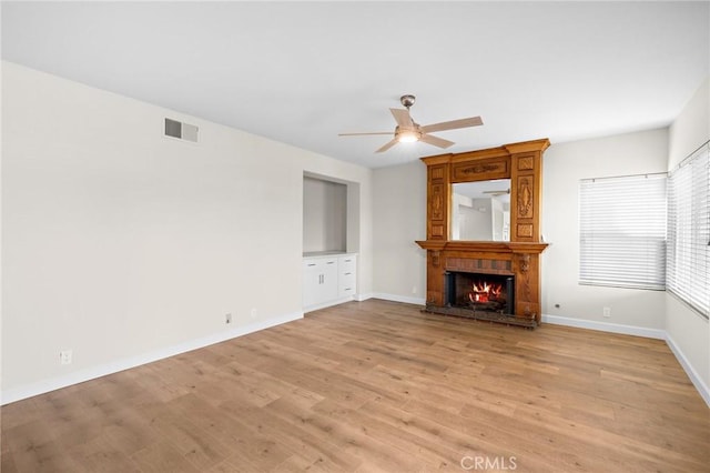 unfurnished living room with baseboards, visible vents, light wood finished floors, ceiling fan, and a brick fireplace