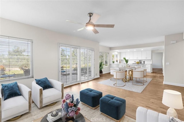 living room with light wood-style flooring, baseboards, and ceiling fan