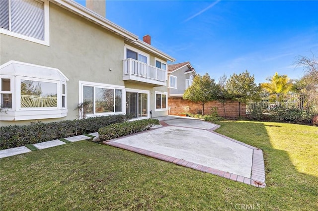 rear view of property featuring fence, stucco siding, a chimney, a balcony, and a patio area