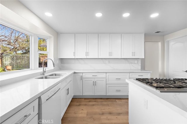 kitchen with light wood finished floors, backsplash, stainless steel gas cooktop, dishwasher, and a sink