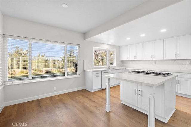 kitchen featuring baseboards, stainless steel gas cooktop, light wood-type flooring, light countertops, and white dishwasher