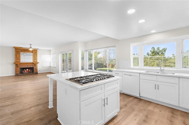 kitchen featuring light wood-style floors, stainless steel gas stovetop, white cabinets, white dishwasher, and a sink