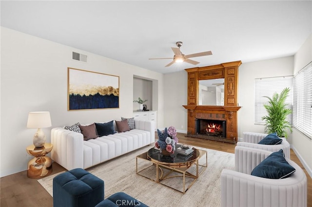 living area with a ceiling fan, a brick fireplace, wood finished floors, and visible vents