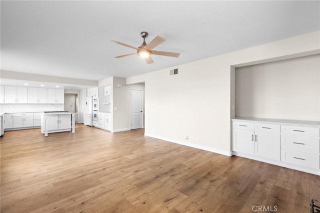 unfurnished living room with light wood-type flooring, visible vents, baseboards, and ceiling fan