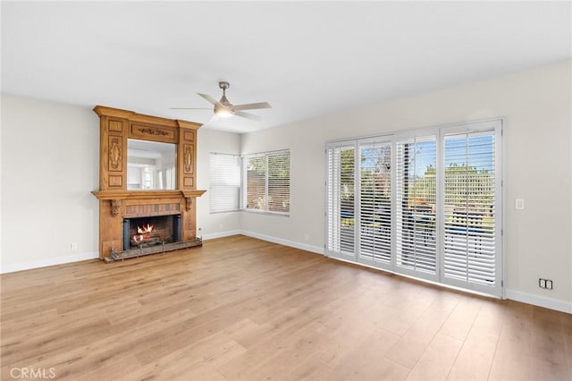 unfurnished living room featuring a large fireplace, baseboards, light wood-style floors, and ceiling fan