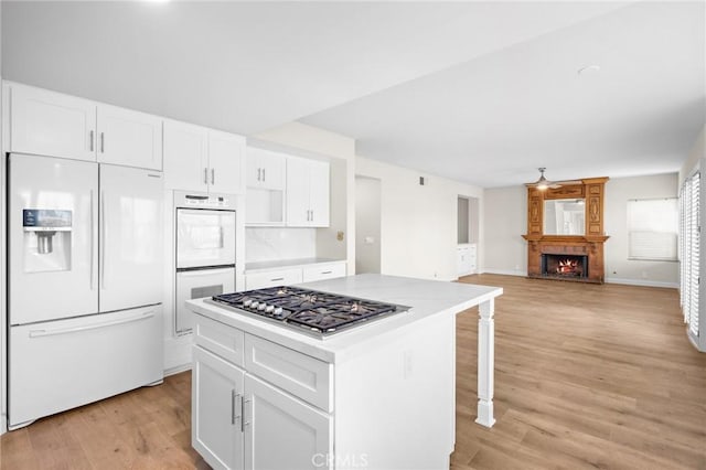 kitchen featuring a kitchen island, light countertops, light wood-style floors, white appliances, and white cabinetry