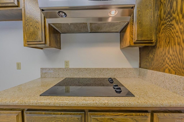 kitchen with black electric stovetop, ventilation hood, and light stone countertops