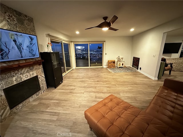 living room with ceiling fan, a stone fireplace, and light hardwood / wood-style floors