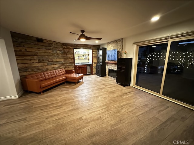 sitting room with ceiling fan, a stone fireplace, and hardwood / wood-style floors