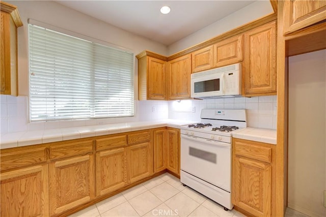 kitchen with white appliances, light tile patterned floors, tile countertops, and tasteful backsplash