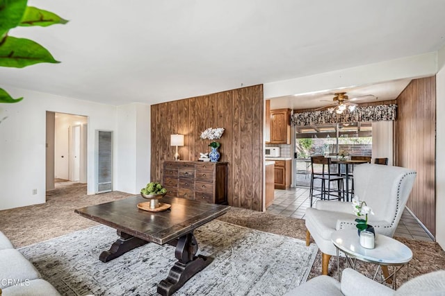 living room with ceiling fan, wooden walls, and light carpet