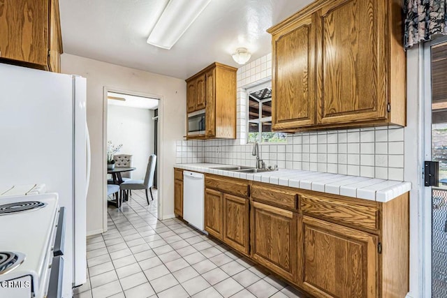 kitchen with sink, white appliances, light tile patterned floors, tile counters, and decorative backsplash