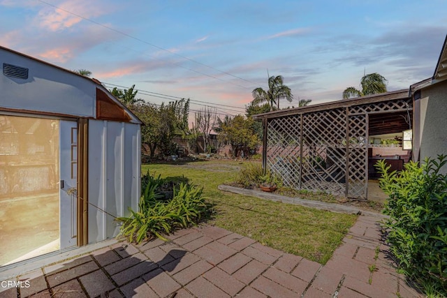 yard at dusk featuring an outdoor structure and a patio area