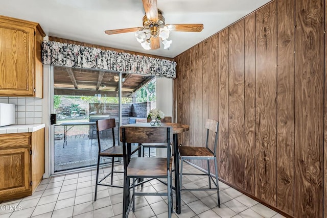 tiled dining area with ceiling fan and wood walls