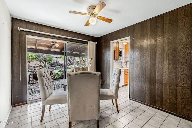 dining space featuring light tile patterned flooring, sink, ceiling fan, and wood walls