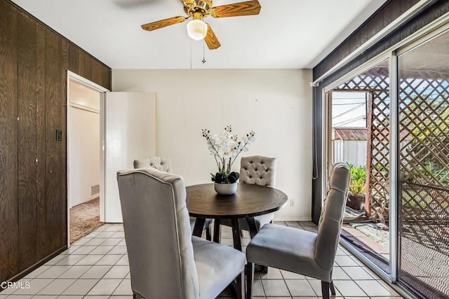 dining space with wooden walls, light tile patterned floors, and ceiling fan