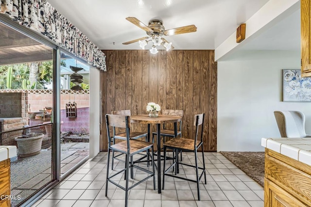 dining room with ceiling fan, wooden walls, and light tile patterned floors