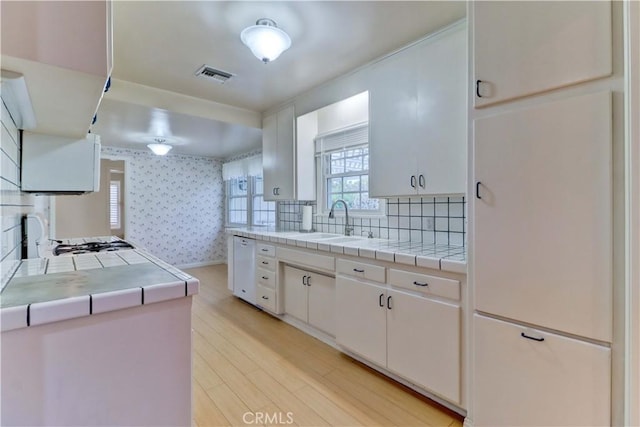 kitchen with sink, dishwasher, tile counters, light hardwood / wood-style floors, and white cabinets