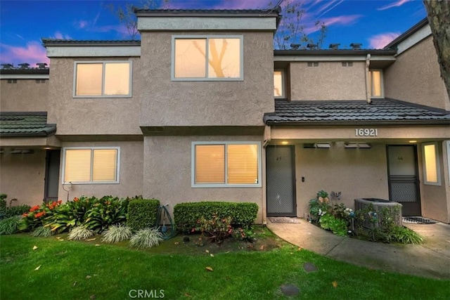 back of house at dusk featuring cooling unit, a yard, and stucco siding