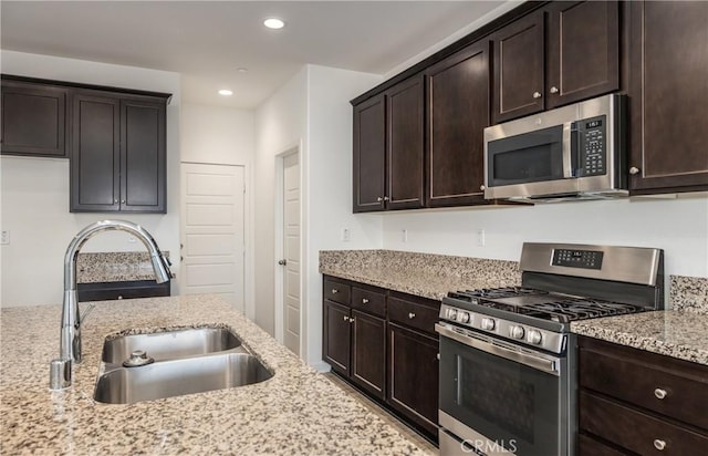 kitchen with light stone counters, appliances with stainless steel finishes, sink, and dark brown cabinets