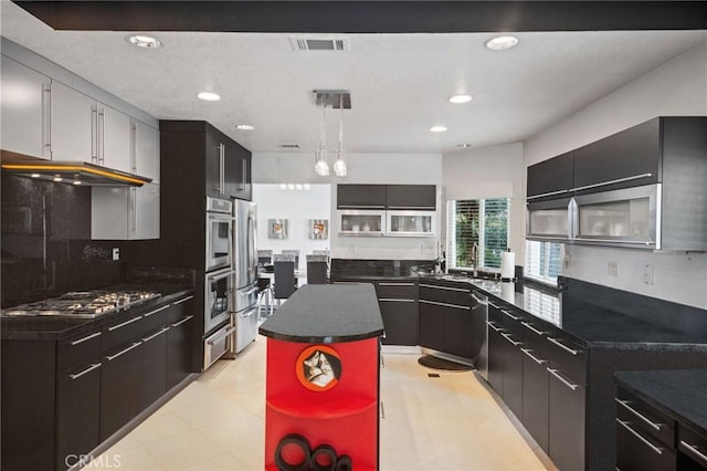 kitchen with a kitchen island, appliances with stainless steel finishes, sink, backsplash, and hanging light fixtures