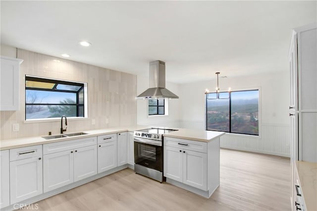 kitchen featuring electric stove, sink, hanging light fixtures, island exhaust hood, and kitchen peninsula