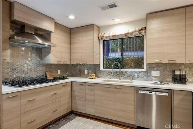 kitchen with appliances with stainless steel finishes, sink, backsplash, light brown cabinets, and wall chimney exhaust hood