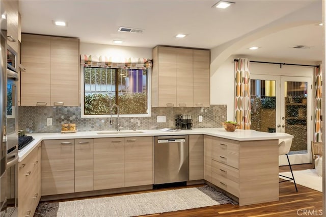 kitchen with sink, appliances with stainless steel finishes, a kitchen bar, light brown cabinetry, and kitchen peninsula