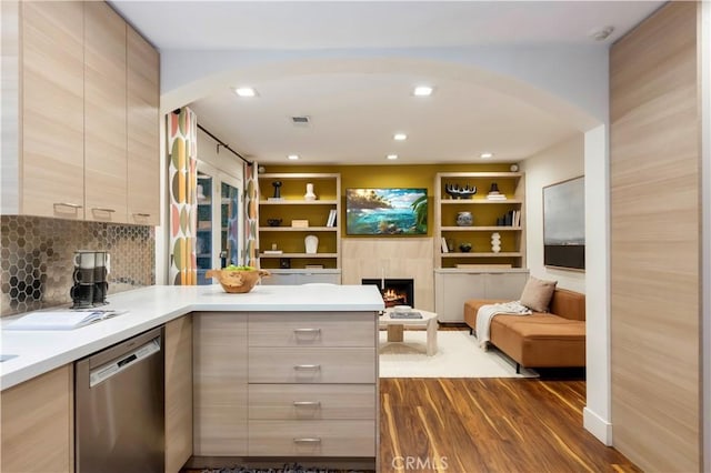 kitchen featuring dark wood-type flooring, dishwasher, a tiled fireplace, light brown cabinetry, and kitchen peninsula