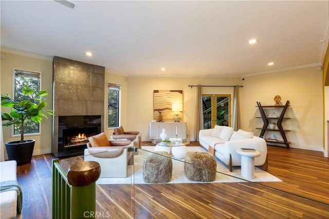 living room with a tiled fireplace, crown molding, and hardwood / wood-style floors