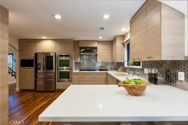 kitchen featuring dark wood-type flooring, light brown cabinetry, sink, appliances with stainless steel finishes, and wall chimney range hood