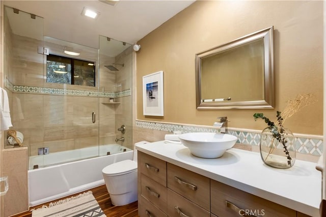 full bathroom with bath / shower combo with glass door, tile walls, hardwood / wood-style flooring, vanity, and toilet