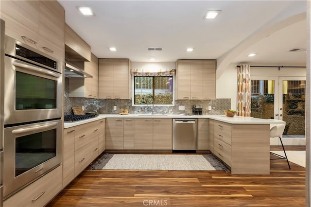 kitchen featuring appliances with stainless steel finishes, light brown cabinetry, sink, a kitchen breakfast bar, and kitchen peninsula