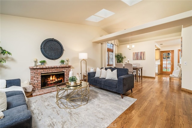 living room with wood-type flooring, a brick fireplace, vaulted ceiling with skylight, and a notable chandelier