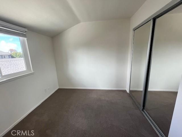 unfurnished bedroom with dark carpet, vaulted ceiling, and a closet