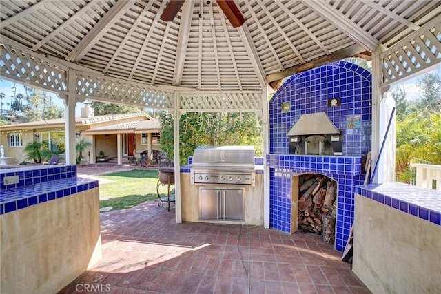 view of patio with a gazebo, a tile fireplace, ceiling fan, a grill, and exterior kitchen