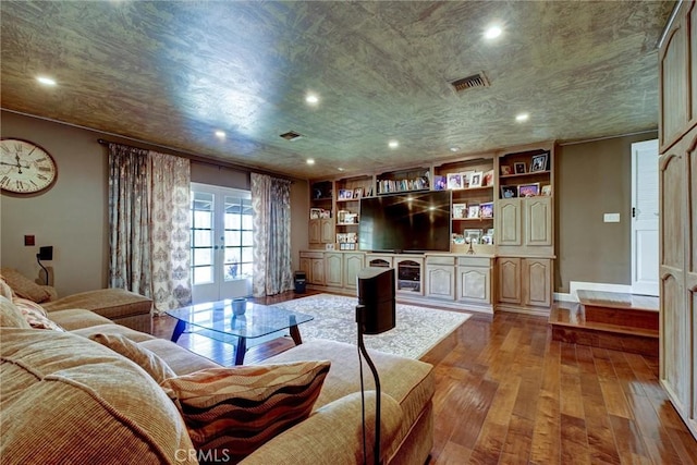 living room featuring built in features, light hardwood / wood-style floors, french doors, and a textured ceiling