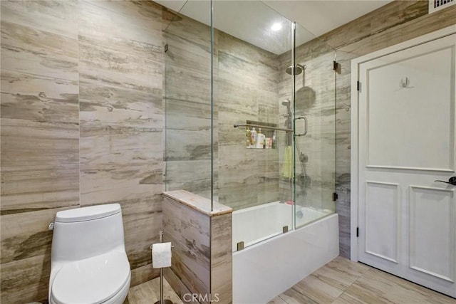 bathroom featuring tile walls, enclosed tub / shower combo, and toilet