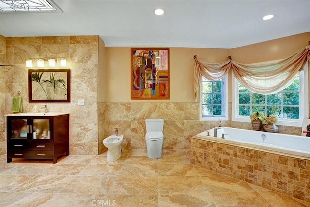 bathroom featuring tile walls, vanity, toilet, tiled tub, and a bidet