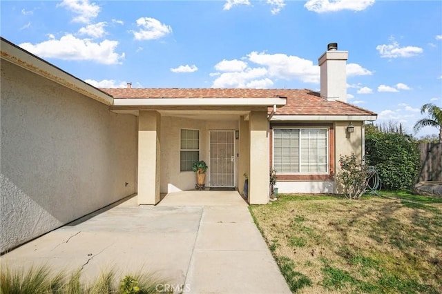 property entrance with roof with shingles, a patio, a yard, a chimney, and stucco siding