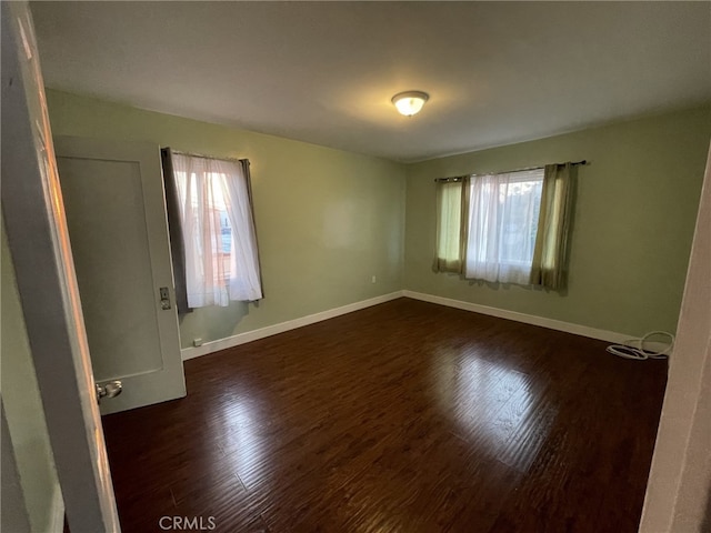 empty room featuring baseboards and dark wood-type flooring