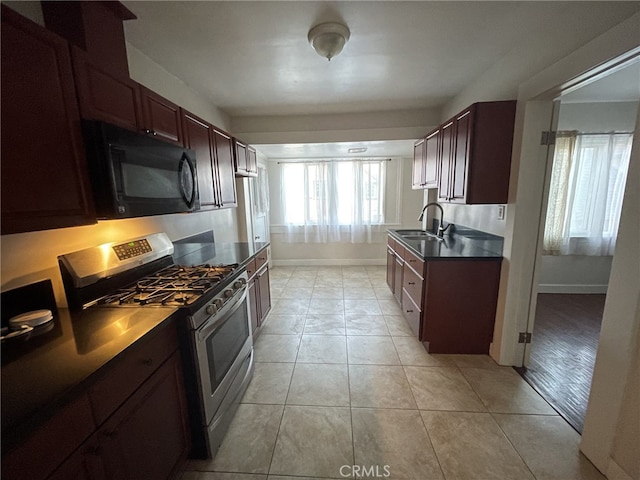 kitchen with light tile patterned floors, dark countertops, a sink, black microwave, and gas range