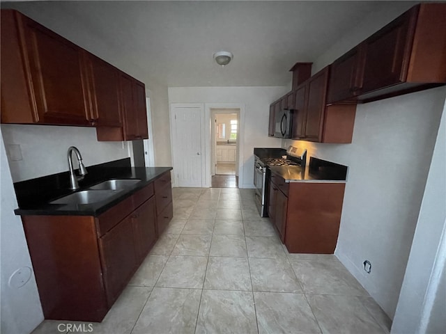 kitchen with a sink, dark countertops, black microwave, light tile patterned floors, and stainless steel range with gas stovetop