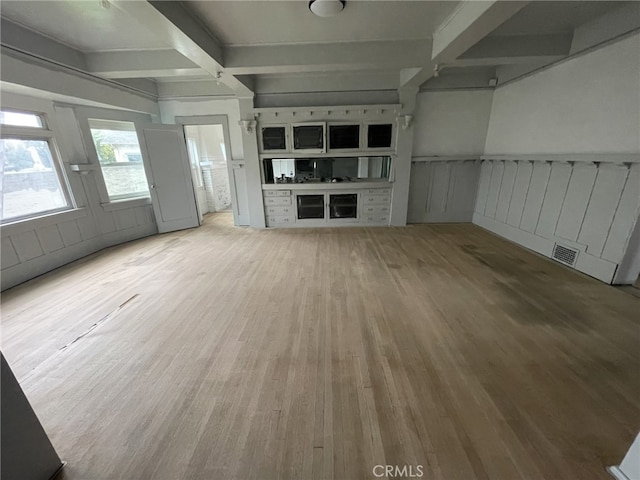 unfurnished living room featuring beamed ceiling, a wainscoted wall, visible vents, and wood finished floors