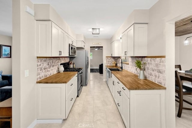 kitchen featuring white cabinetry, butcher block counters, appliances with stainless steel finishes, and a sink