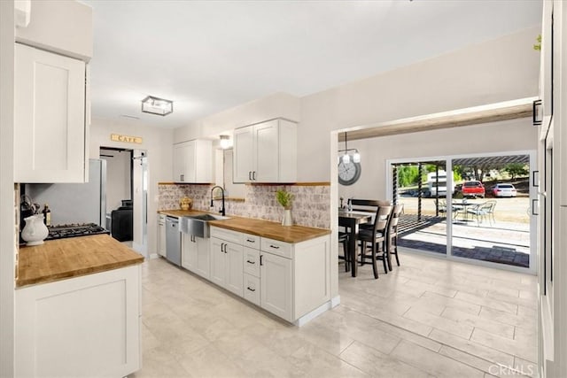 kitchen with wooden counters, stainless steel dishwasher, a sink, and white cabinets