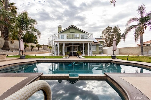 rear view of property with a balcony, a pool with connected hot tub, fence, and a patio