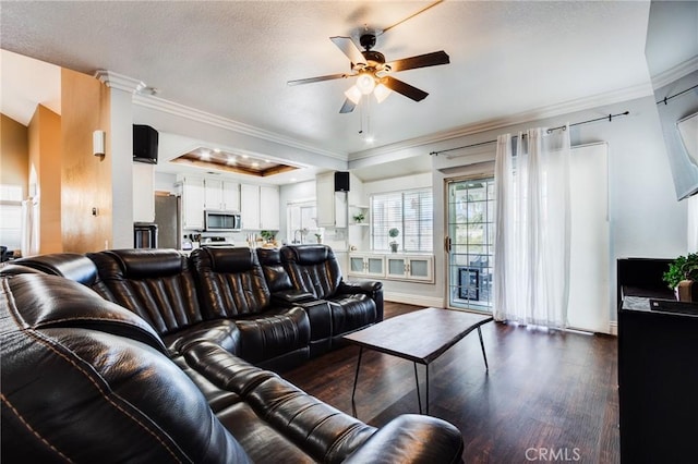 living room with a textured ceiling, dark wood-style flooring, a ceiling fan, a tray ceiling, and crown molding