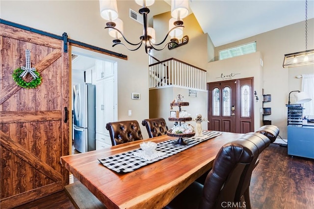 dining space featuring visible vents, a towering ceiling, a barn door, dark wood-type flooring, and a chandelier